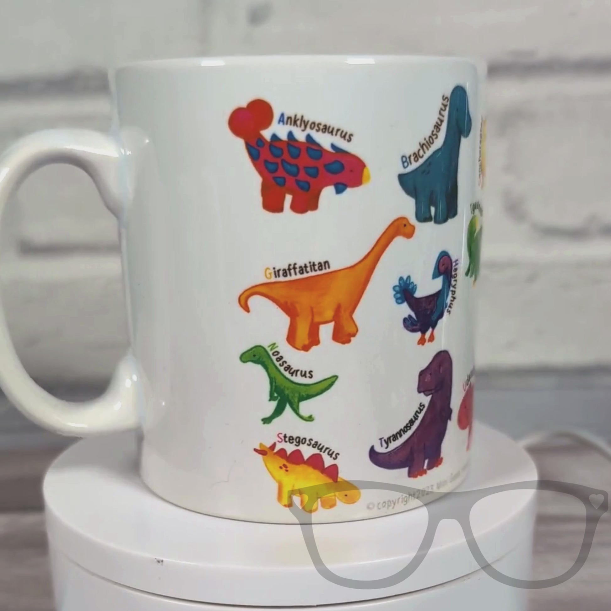 Video of A to Z Dinosaur Mug rotating on a turntable, showcasing full-colour dino illustrations on a white ceramic surface