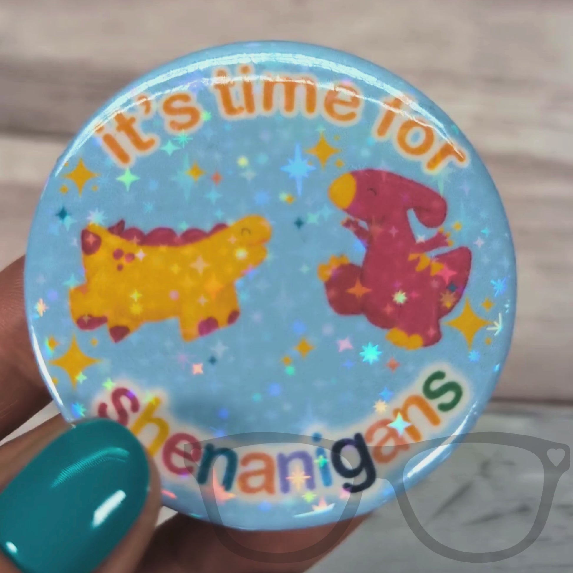 Watch the "It’s Time for Shenanigans" sparkling badge come to life in this close-up video! See how the glitter catches the light, creating a dazzling shimmer that adds fun and flair to any outfit or accessory. Perfect for fans who love a bit of sparkle with their geeky style, this badge shines bright whether pinned on bags, jackets, or hats.