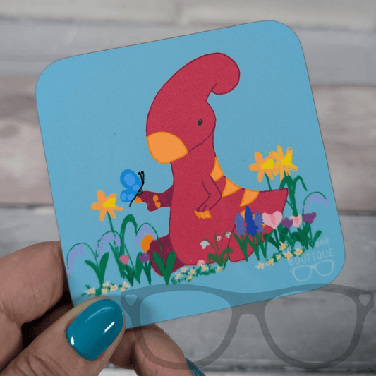 Blue square drink coaster featuring Irene the pink Parasaurolophus in a flower field, Mini Geek Boutique kids’ coaster.