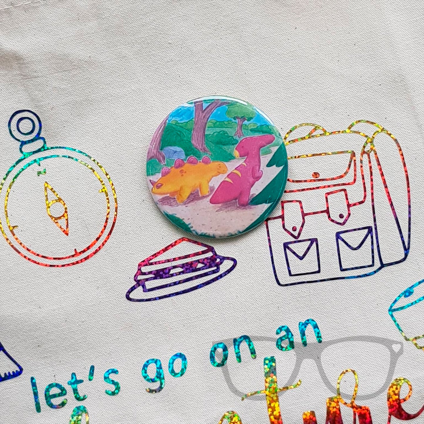 This 58mm badge shows the illustration of Derek and Irene the dinosaurs starting off on their adventure.
