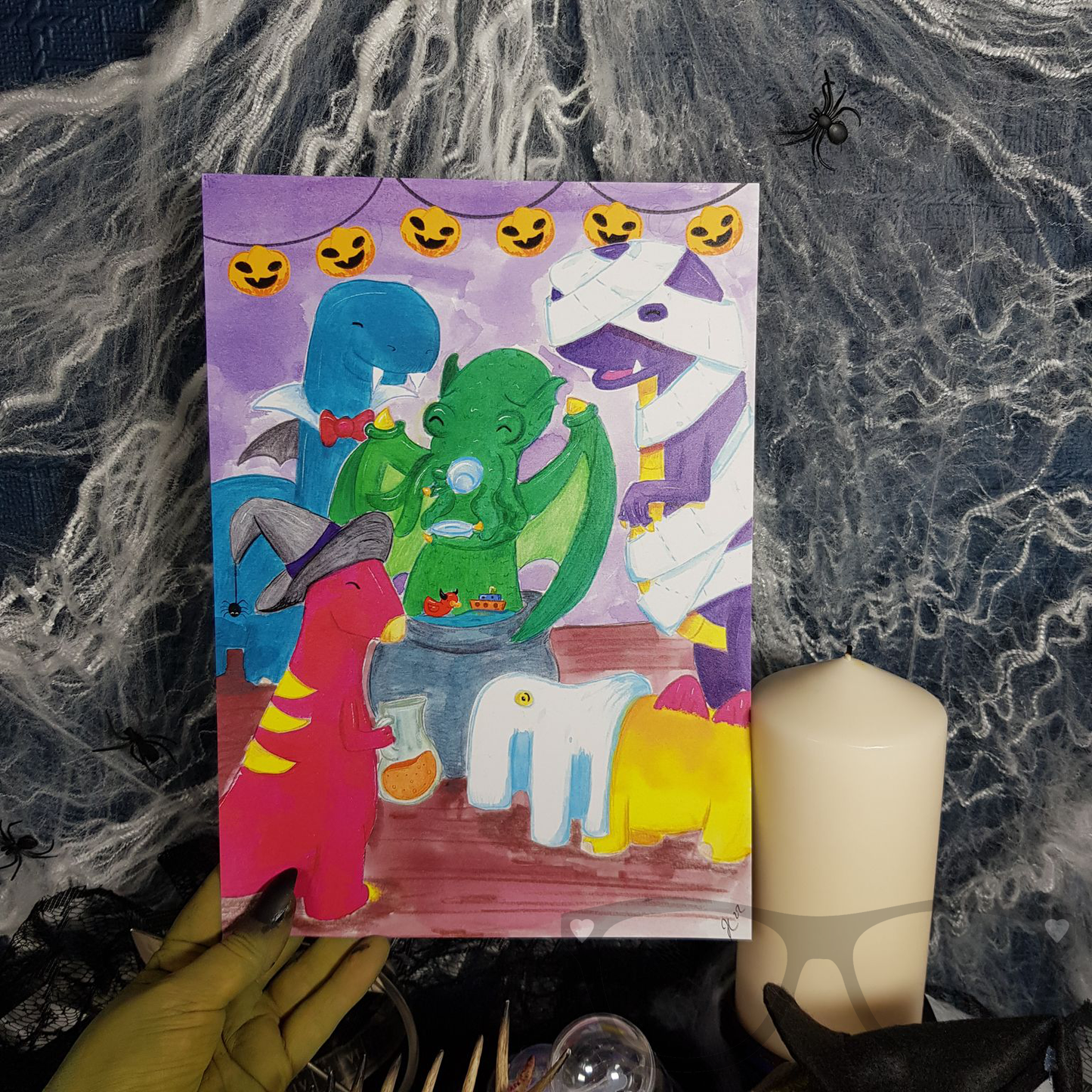 Halloween dinosaur art print A4 being held by a witchy hand. A digital print based on an original illustration by Mini Geek Boutique
