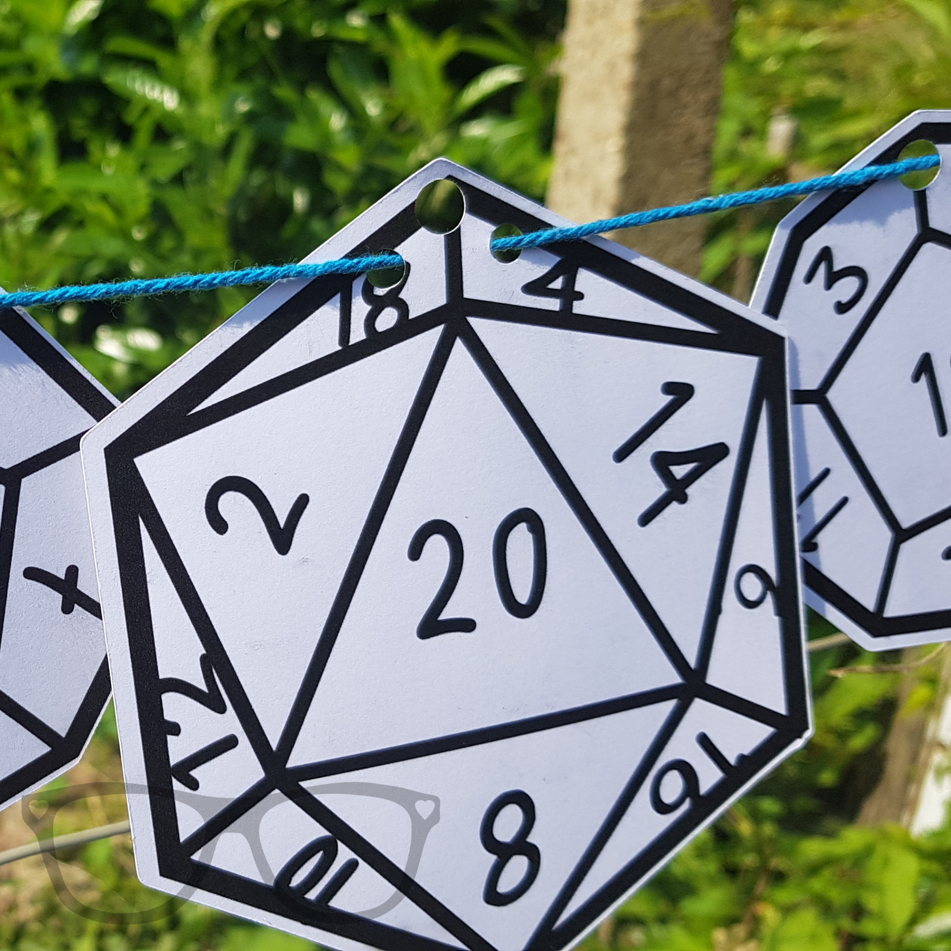 Colour-in polyhedral dice bunting displayed, including Nat 20 and Nat 1 designs. Ideal for tabletop gamers or D&D-themed parties.
