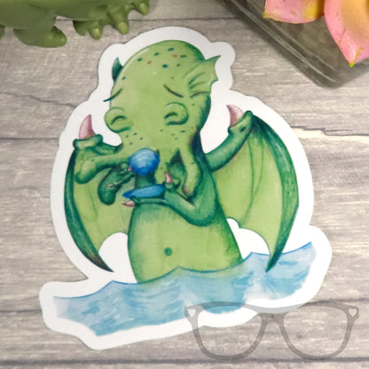 Cthulhu vinyl sticker designed by a fun kawaii illustrator, perfect for geeks and Lovecraft fans. Features Cthulhu drinking tea, making it a quirky and unique gift.