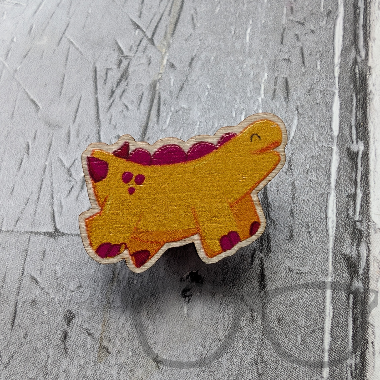 Wooden pin showing a full colour design of Derek the yellow stegosaurus