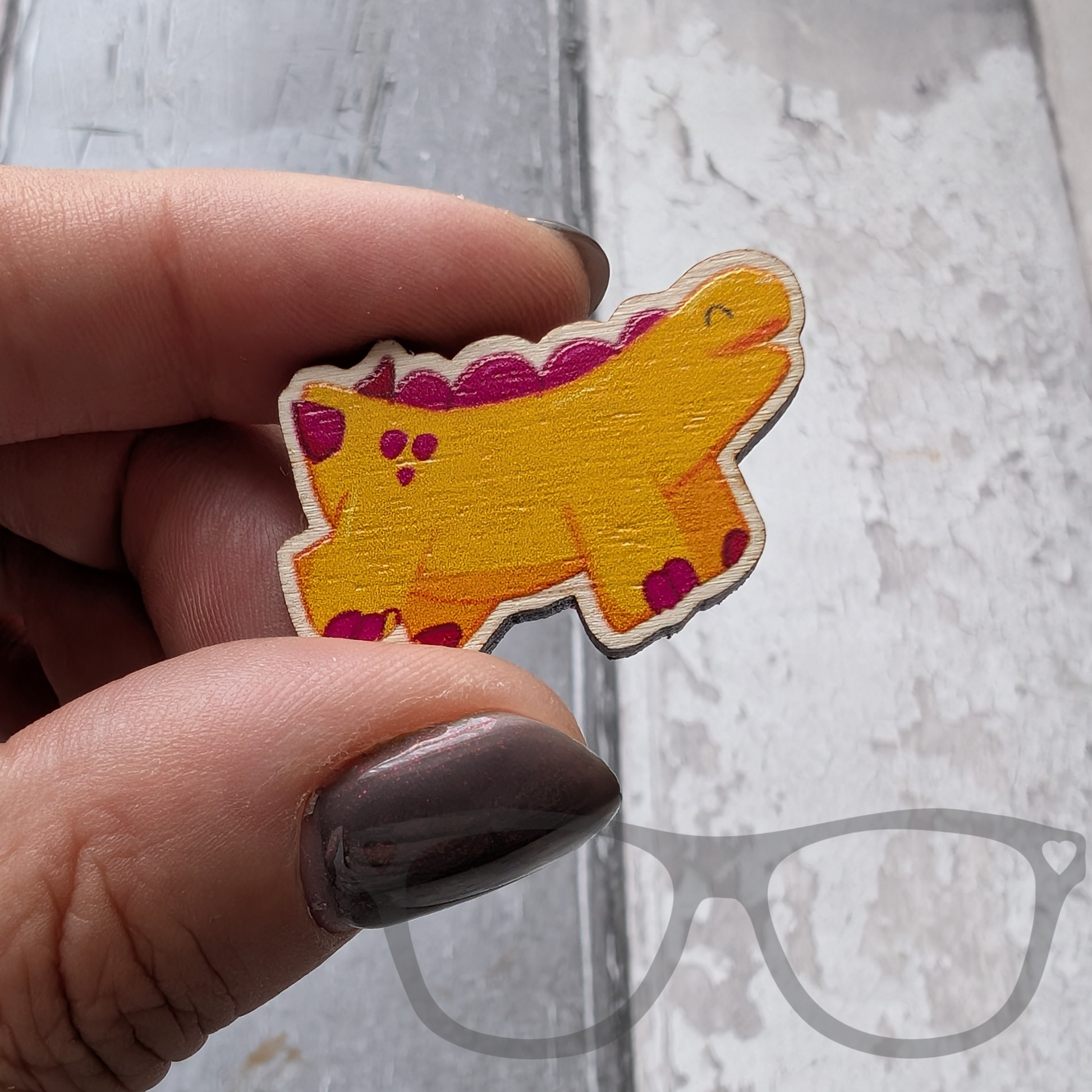 Derek the stegosaurus wooden pin being held to show detail