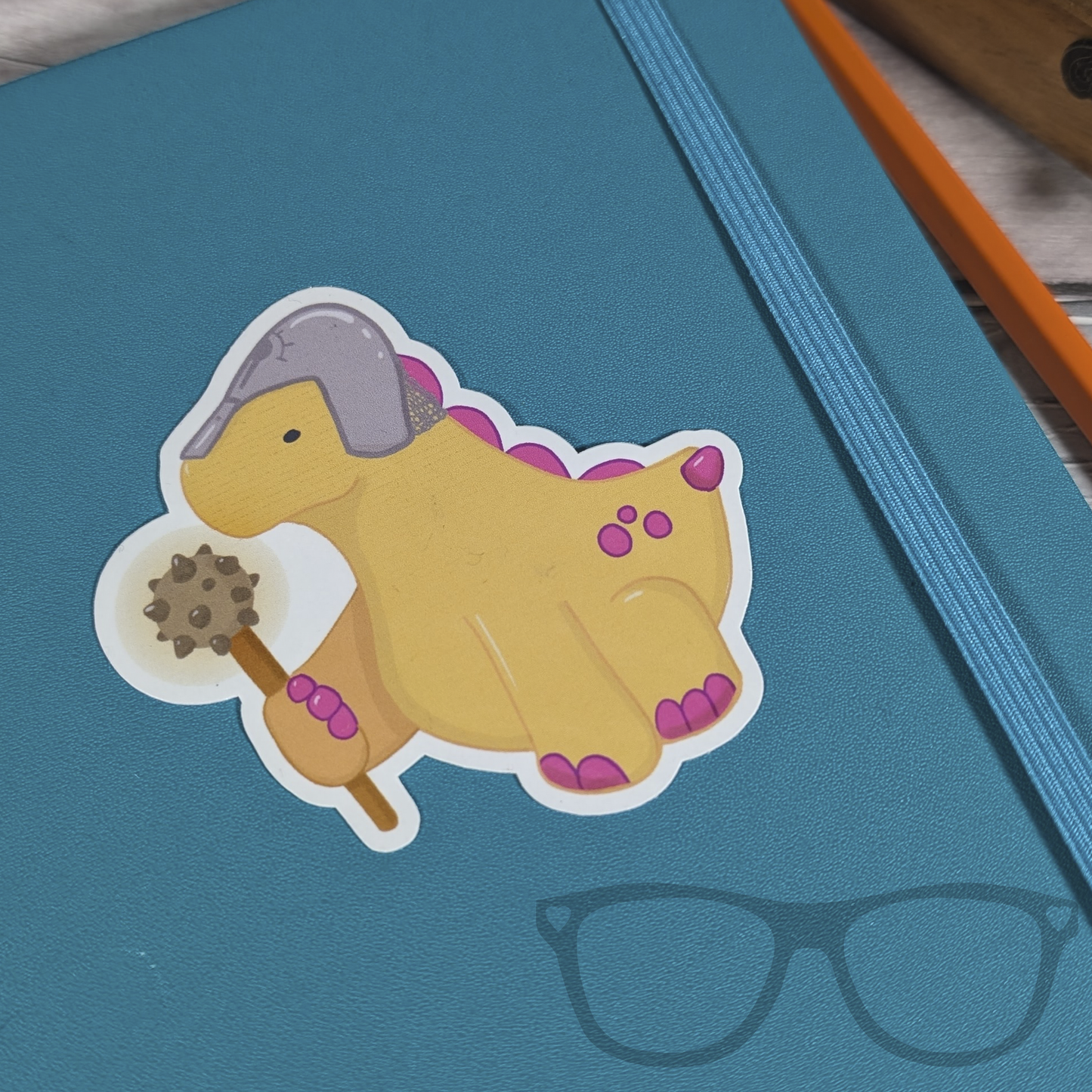 Derek the Cleric Stegosaurus vinyl sticker on a notebook