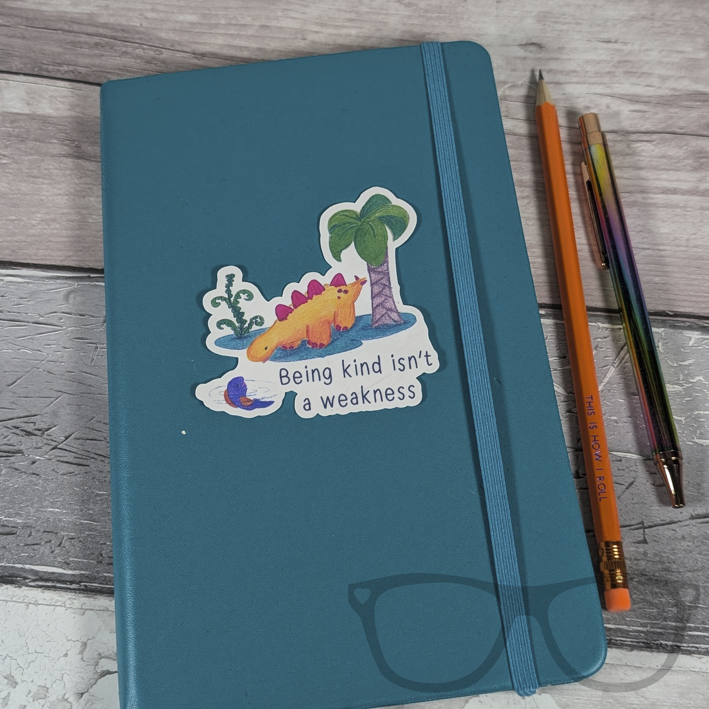 Derek the Stegosaurus kindness vinyl sticker on a notebook, featuring the empowering quote 'Being kind isn't a weakness.' Ideal for decorating books and folders