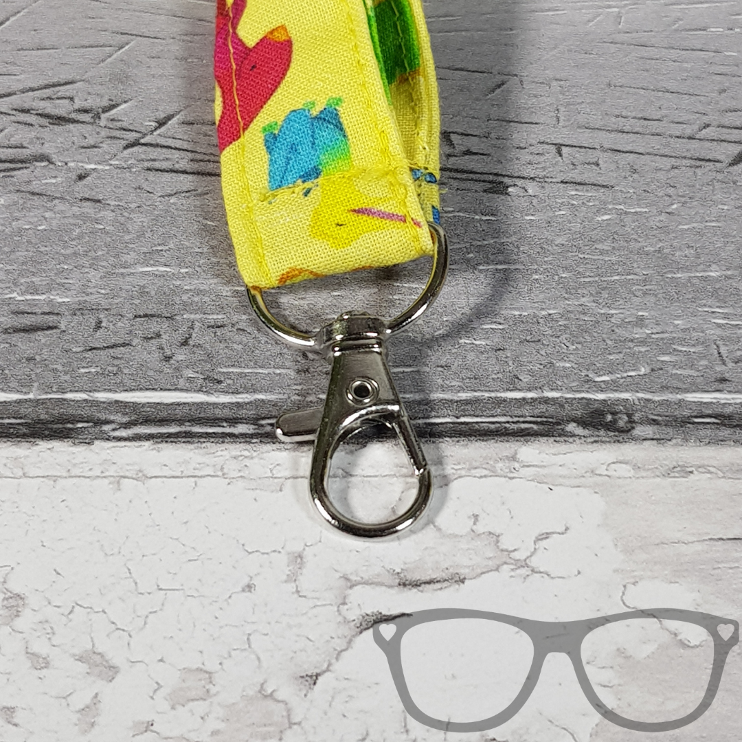 Dinosaur Lanyard, yellow fabric with colourful fun dinosaurs in a pattern. The lanyard features a lobster style clip for your keys or ID Card, and a quick release safety clip