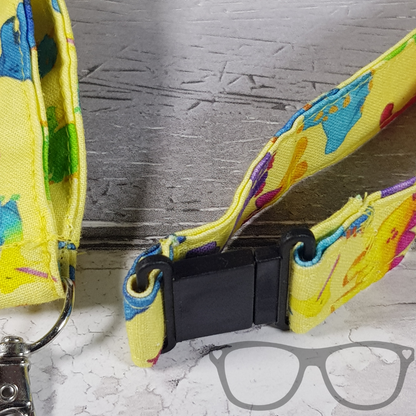 Dinosaur Lanyard, yellow fabric with colourful fun dinosaurs in a pattern. The lanyard features a lobster style clip for your keys or ID Card, and a quick release safety clip