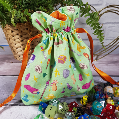 Light green Drawstring bag ideal for carrying dice, minis, snacks and little trinkets. Light green fabric with icons of fantasy genre, lined with a contrasting orange fabric and secured using an orange ribbon