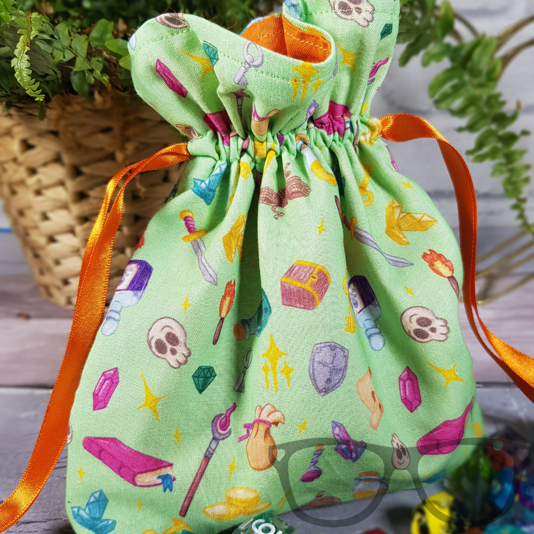 Light green Drawstring bag ideal for carrying dice, minis, snacks and little trinkets. Light green fabric with icons of fantasy genre, lined with a contrasting orange fabric and secured using an orange ribbon