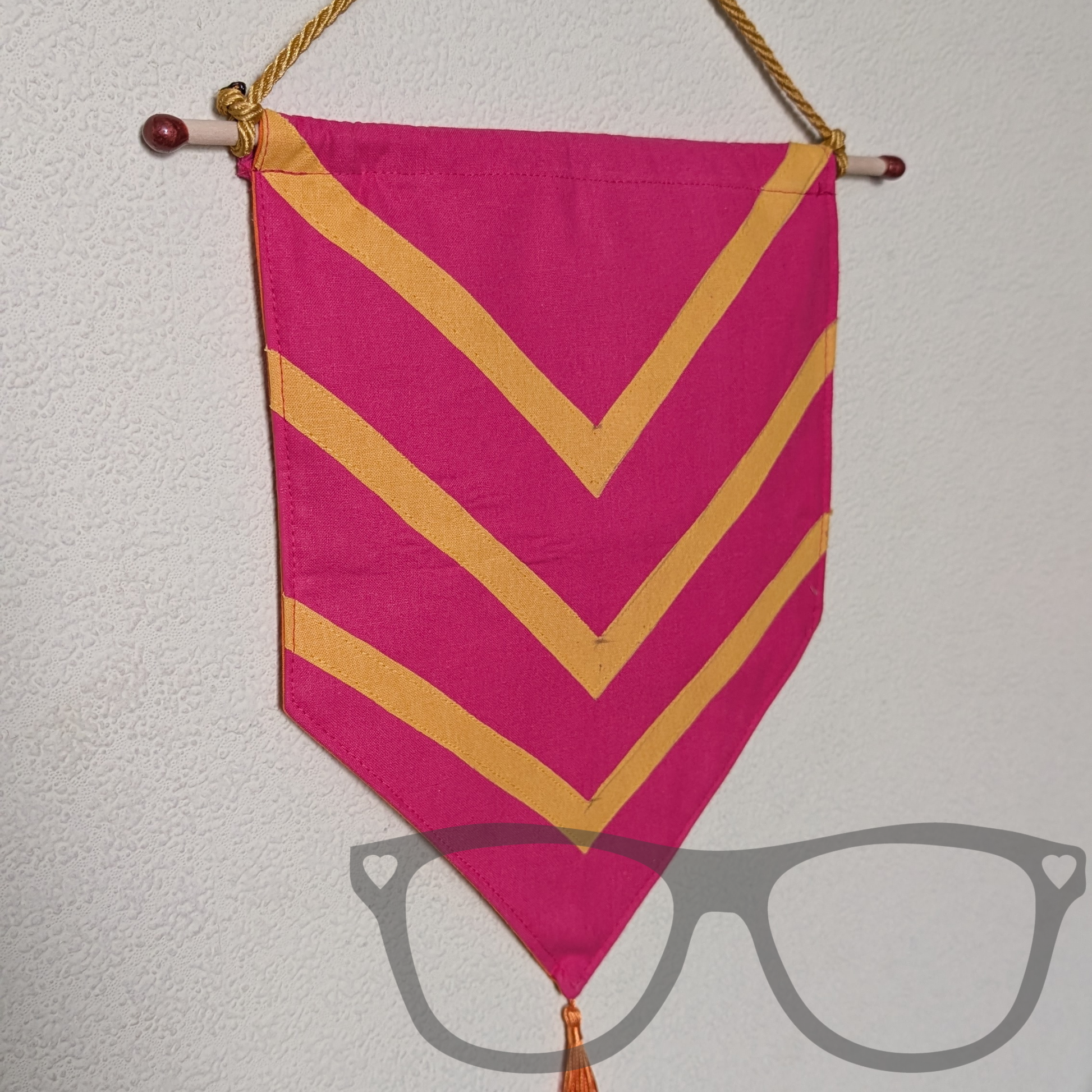 Bright pink medieval style banner with 3 yellow arrow stripes on, hung by a gold cord and finished with a gold yellow tassel