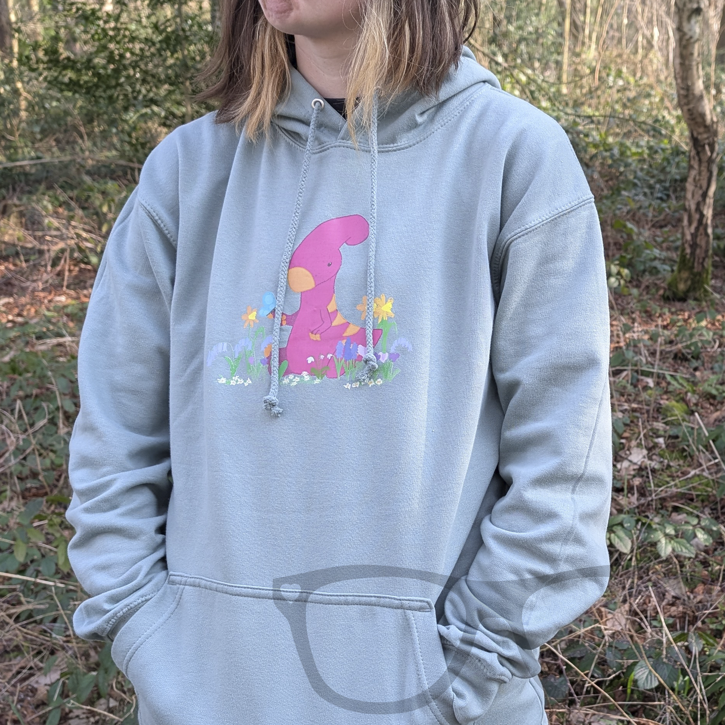 A full view of the dusty green hoodie showcasing the Irene the Parasaurolophus spring design. This soft and comfortable dinosaur hoodie is perfect for geeks and dino fans of all ages