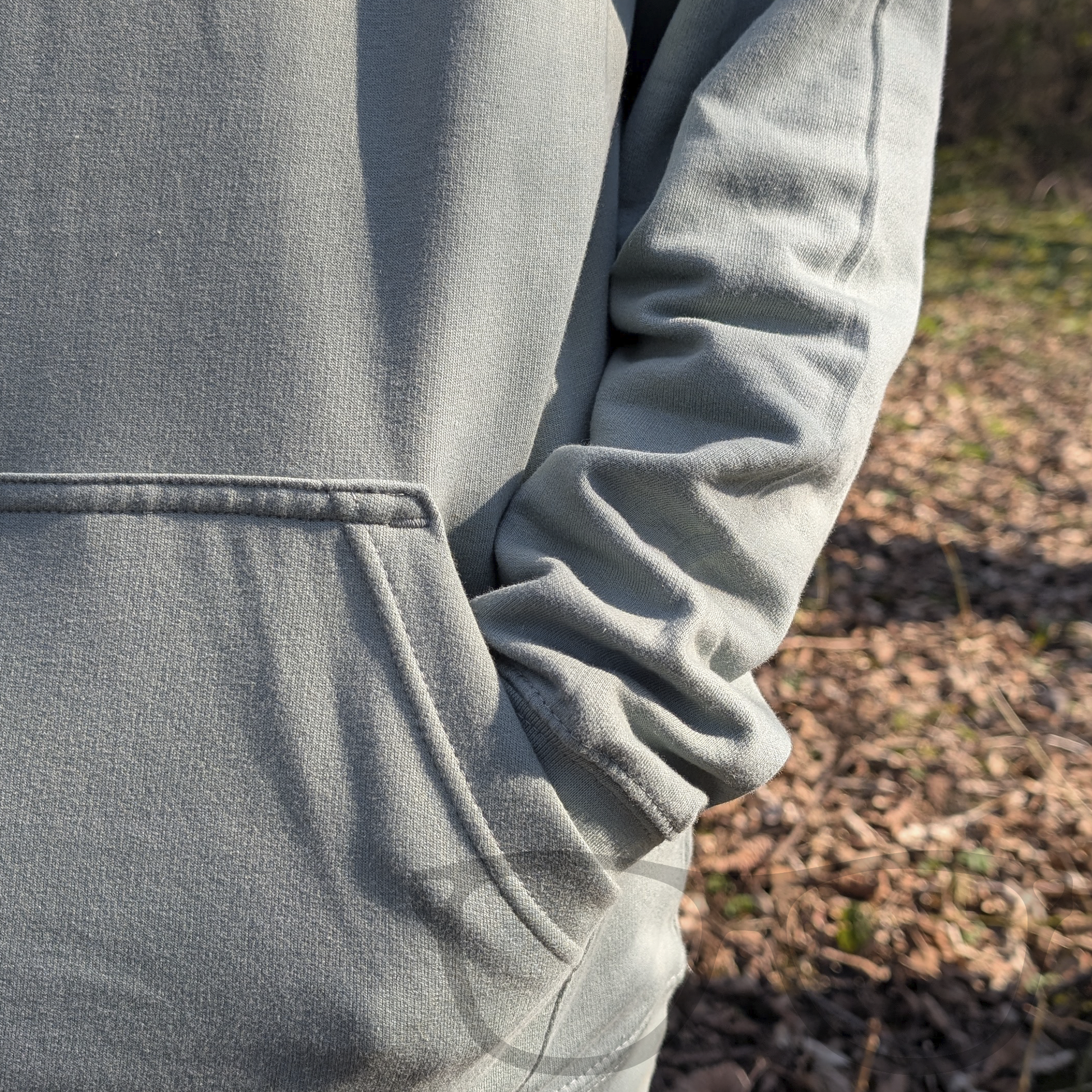 A close-up of the kangaroo pocket on the dusty green dinosaur hoodie, featuring Irene the Parasaurolophus in spring flowers. The cosy pocket is perfect for keeping your hands warm.