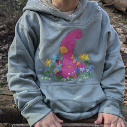A child happily wearing the dusty green dinosaur hoodie featuring Irene the Parasaurolophus in spring flowers. This cosy hoodie is perfect for young dino fans.