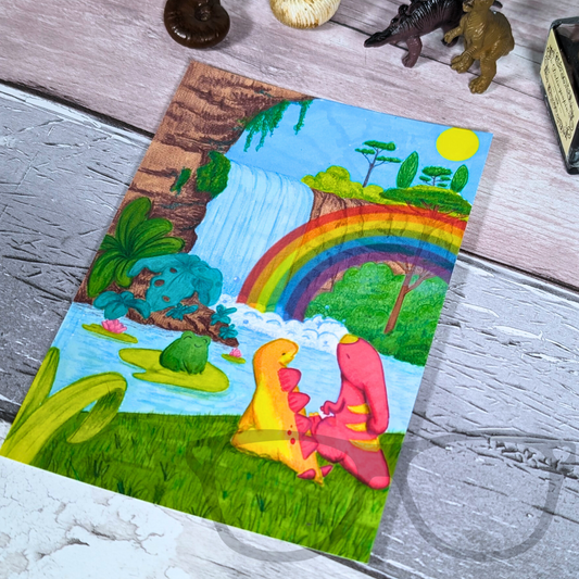 Slightly angled photo to show the colours of the rainbow postcard featuring the dino friends Derek and Irene enjoying a magical rainbow