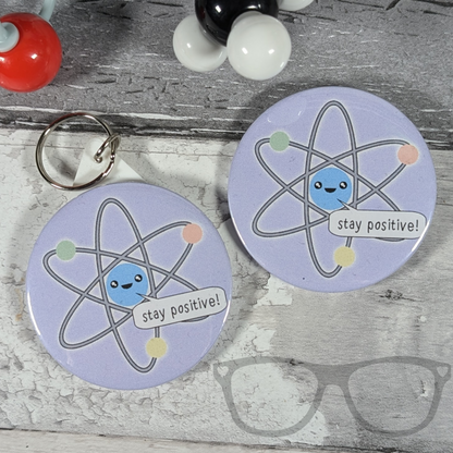 Stay positive atomic science badge and keyring, purple badge with cute kawaii atom saying "Stay Positive"