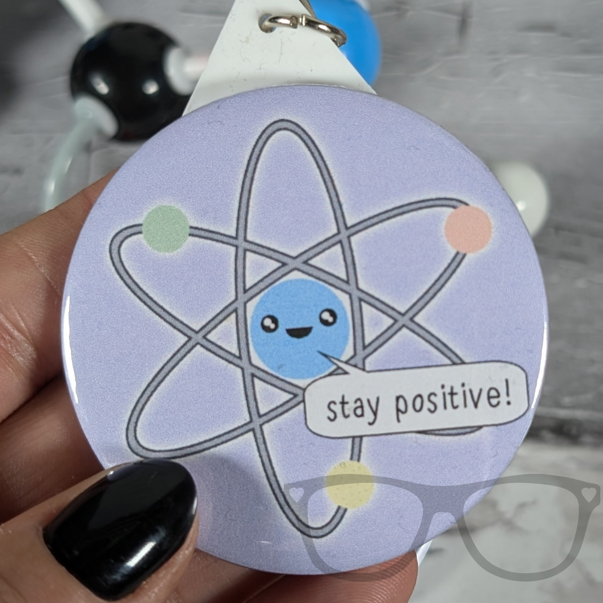 Stay positive atomic science keyring, purple badge with cute kawaii atom saying "Stay Postitive"