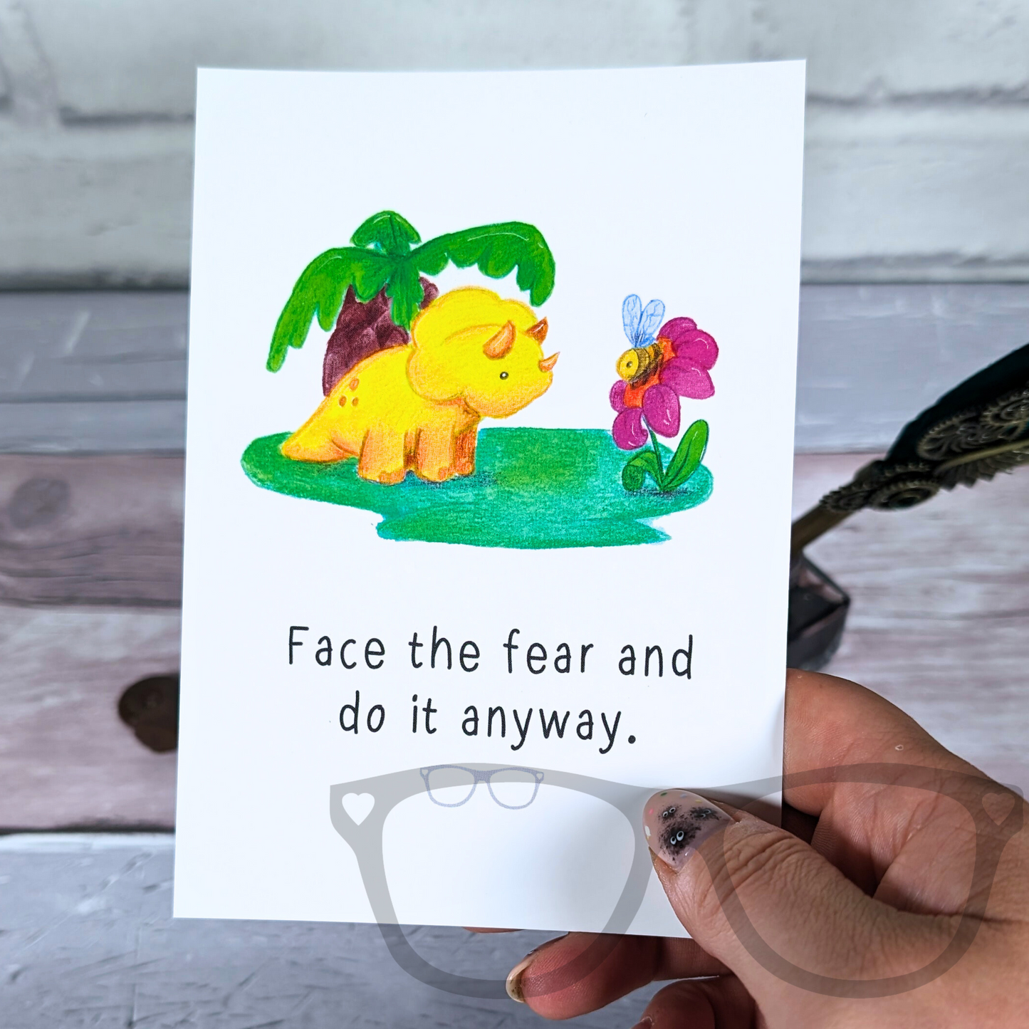 Tracy the triceratops says face the fear and do it anyway. Illustration on a postcard