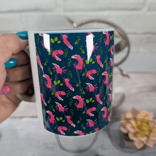 Mug with pink and green axolotl pattern held by a person with blue nail polish.