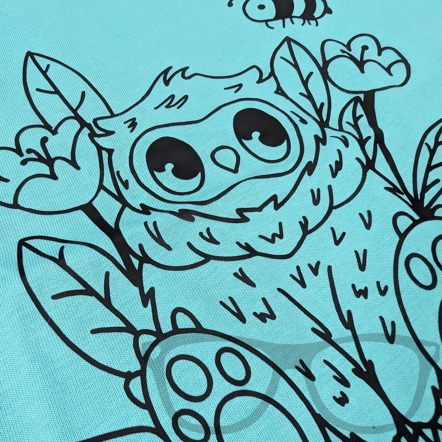 Close-up of the black outline vinyl Owlbear design heat-pressed onto a blue organic cotton T-shirt. Highlights the fine details and clean lines of this fantasy-inspired artwork.