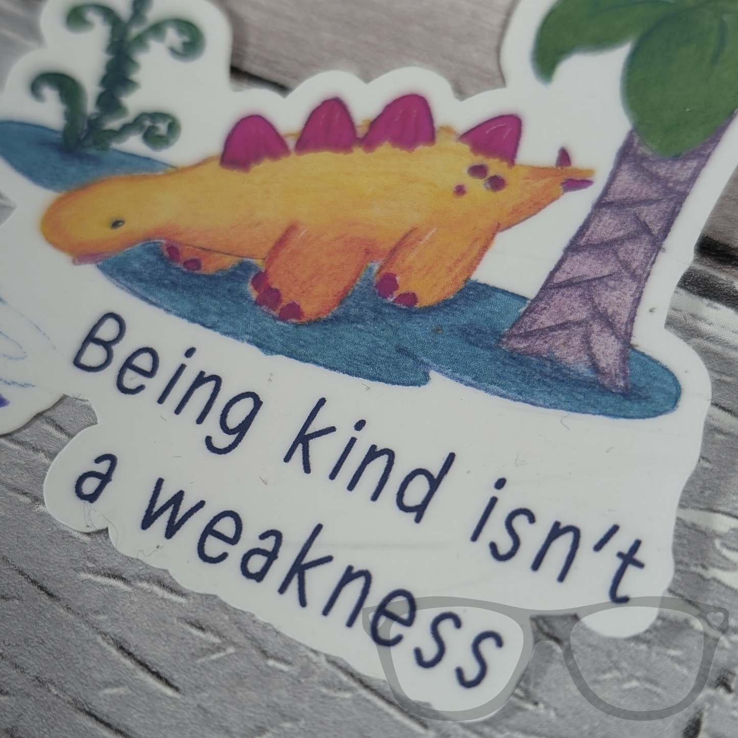 Close-up of Derek the Stegosaurus kindness vinyl sticker with a gloss finish, highlighting the quote 'Being kind isn't a weakness' and watercolour illustration.