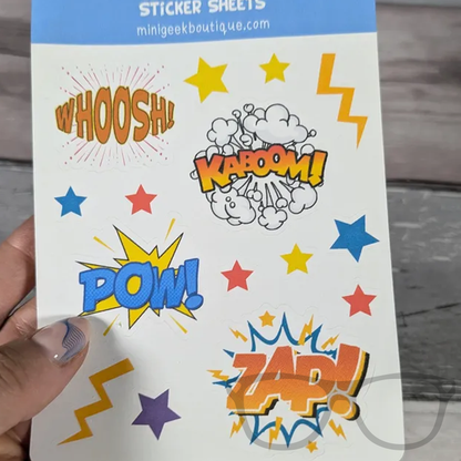 Sticker sheet featuring comic sounds like Pow, Zap, KABOOM, and Woosh, held in hand, perfect for decorating notebooks, journals, and reward charts.