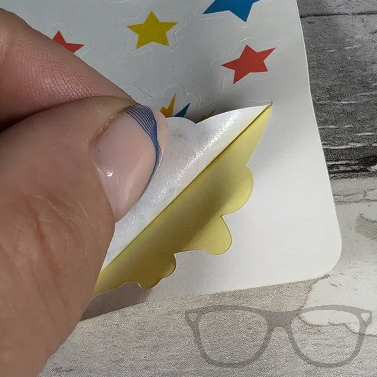 Sticker being lifted off the Comic Sounds sticker sheet, showing how each playful design is easily removable for decorating and journaling.