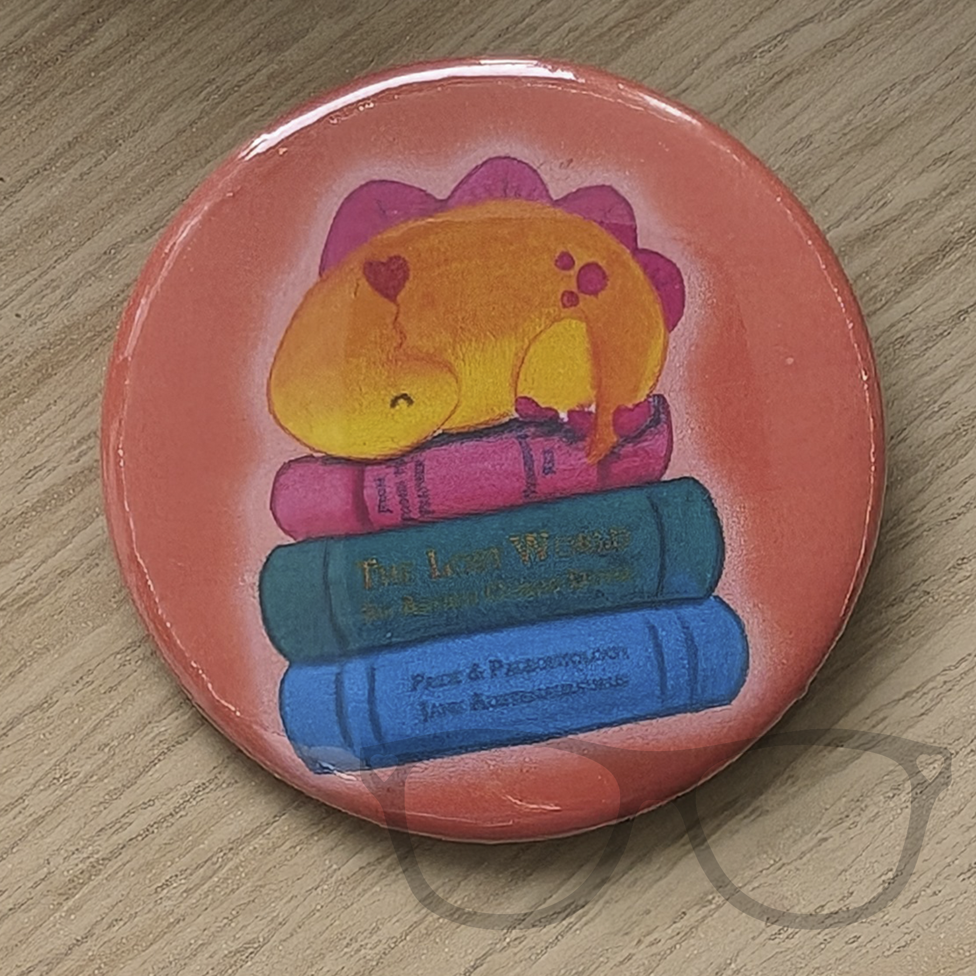 circular 58mm button badge featuring Derek the Stegosaurus napping on some books 