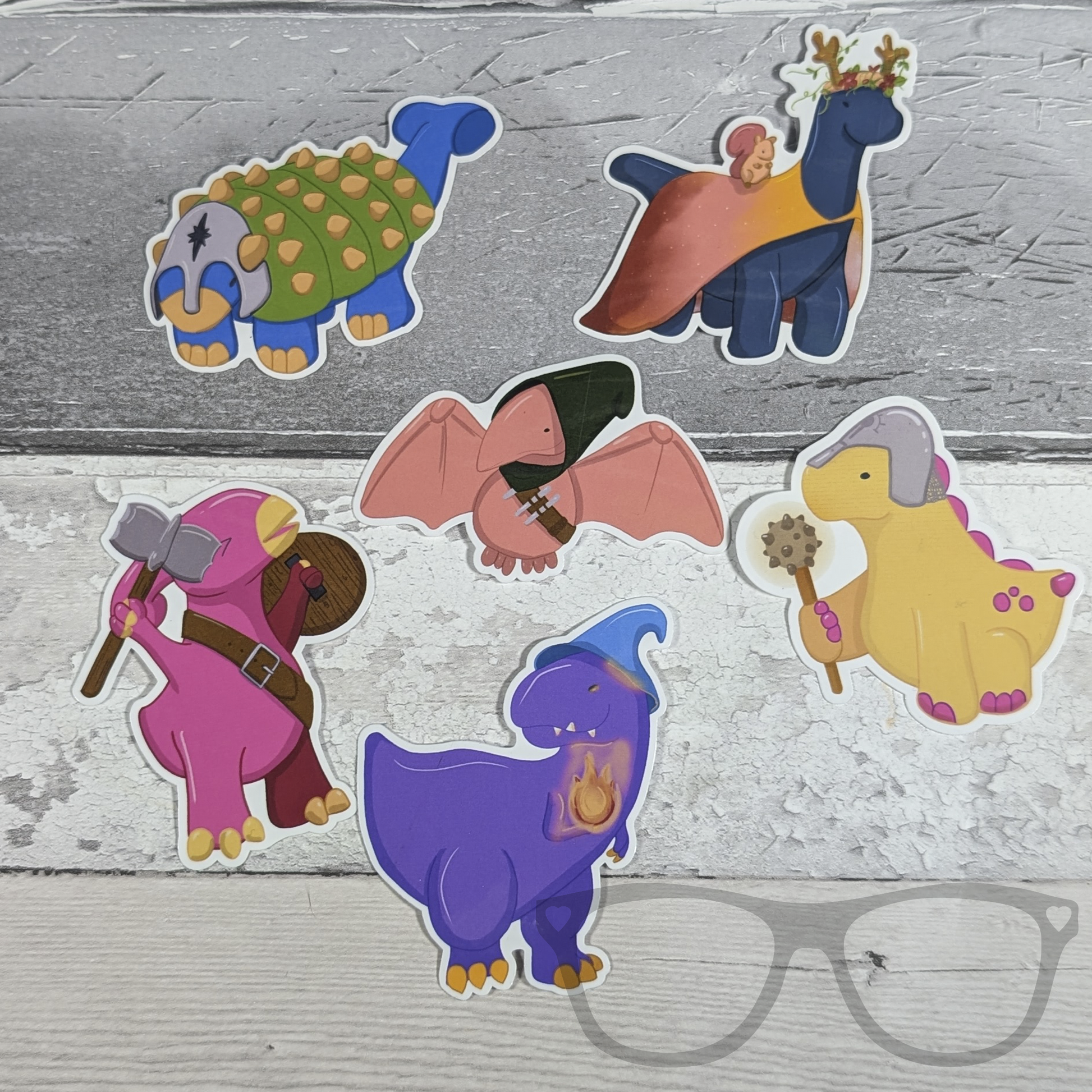 All DnDinos dinosaur vinyl stickers in a group. Pterry the rogue, Derek the Cleric, Irene the Barbarian, Mr Bolan the Wizard, Hank the tank, Brenda the Druid, a great gift idea for  any fan of tabletop roleplaying and dinosaurs.