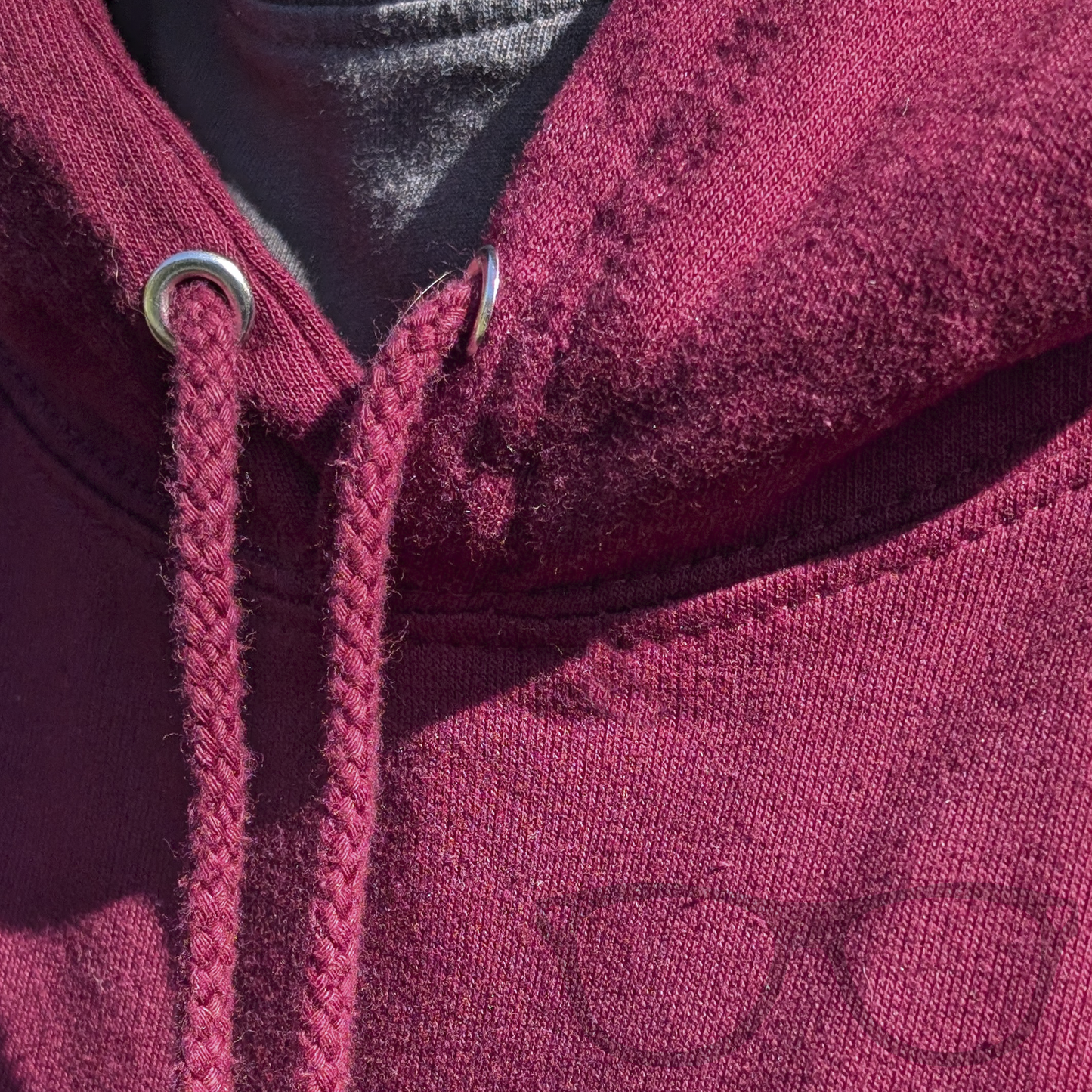 Close-up of pull cord on burgundy hoodie with kangaroo pocket, featuring Derek the Stegosaurus sitting among falling autumn leaves.