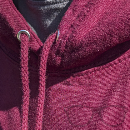 Close-up of pull cord on burgundy hoodie with kangaroo pocket, featuring Derek the Stegosaurus sitting among falling autumn leaves.