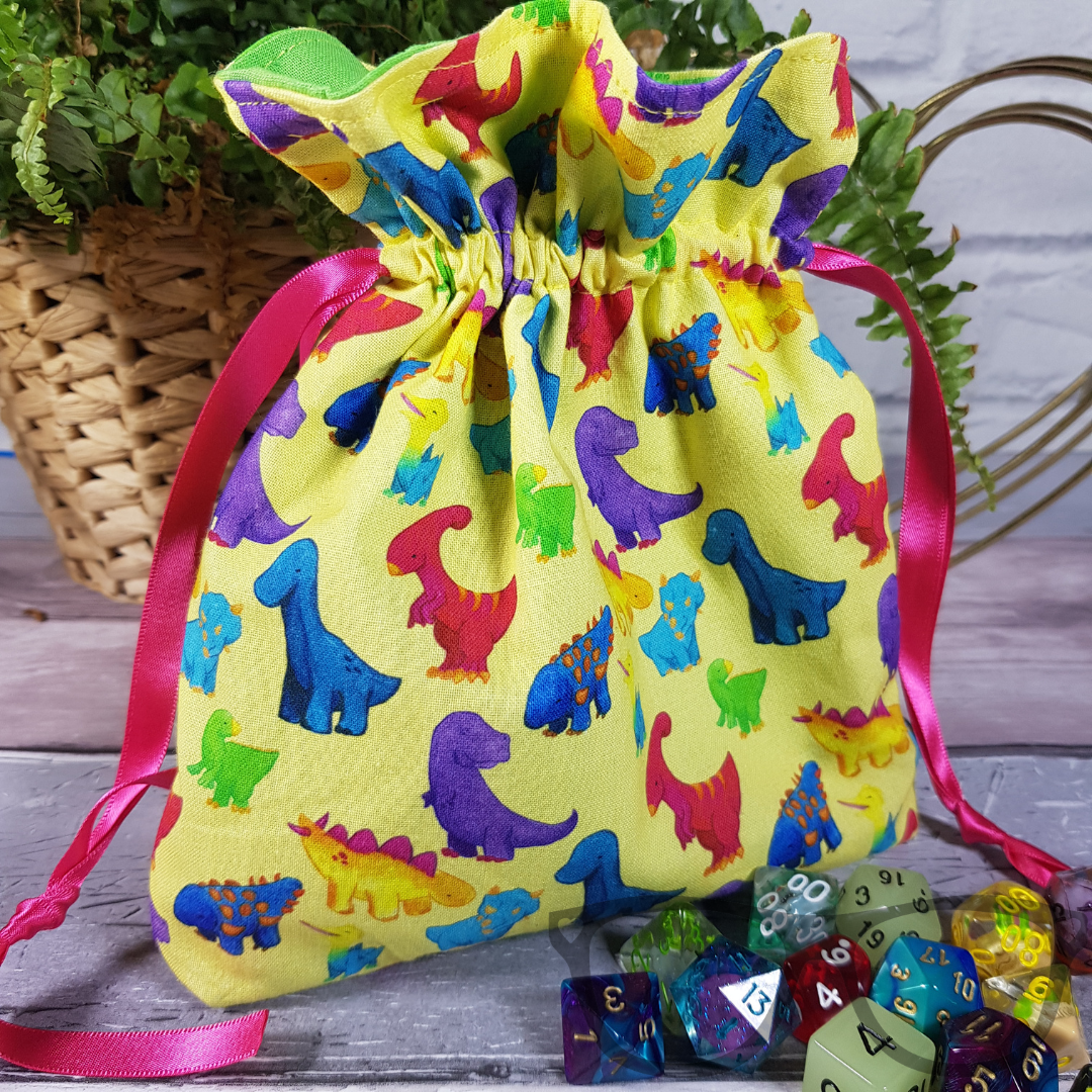 Dinosaur drawstring bag, featuring the dinosaur firiends on a vivid yellow background, lined with a contrasting cotton and secured with pink ribbon, ideal for dice, small toys and more!