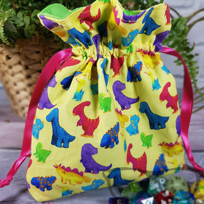 Dinosaur drawstring bag, featuring the dinosaur firiends on a vivid yellow background, lined with a contrasting cotton and secured with pink ribbon, ideal for dice, small toys and more!