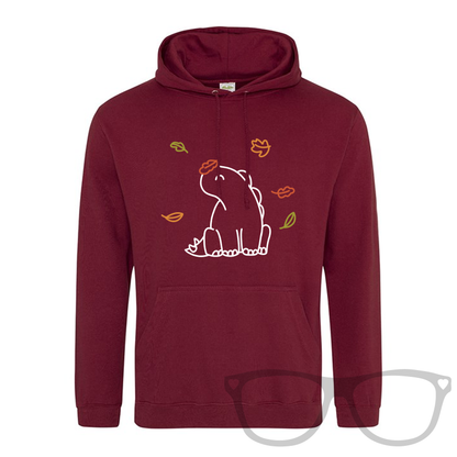 Mock up showing Burgundy Hoodie with kangaroo pocket for Autumn featuring Derek the Stegosaurus sitting amongst the falling autumn leaves