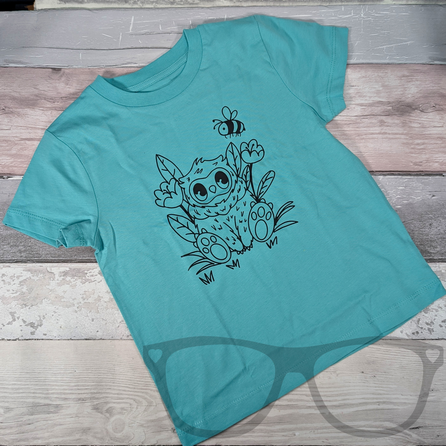 Flat lay of a blue T-shirt featuring the black outline vinyl Owlbear design, heat-pressed onto organic cotton fabric. A stylish and geeky tee perfect for fantasy fans and tabletop gaming enthusiasts.