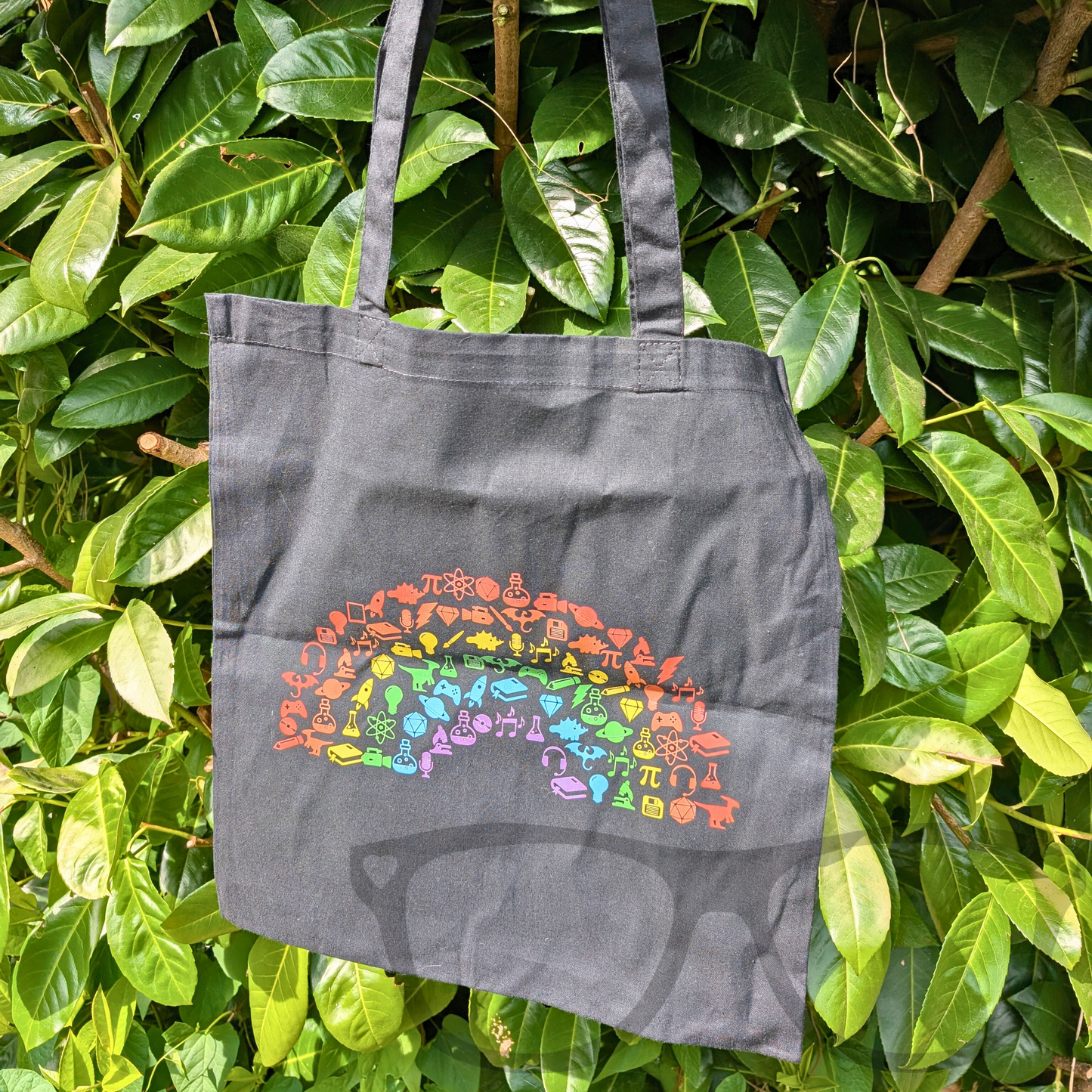 Black cotton tote bag featuring a vibrant rainbow "Geek and Proud" design printed on the front, perfect for gamers and geeks who want to show their pride