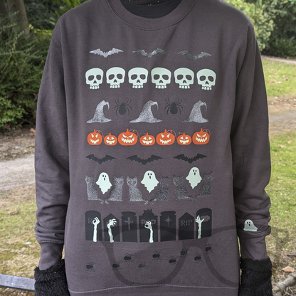 Grey Halloween sweater featuring a variety of spooky graphics including skulls, bats, witches' hats, spiders, and pumpkins with glow-in-the-dark eyes, styled like a traditional ugly sweater.