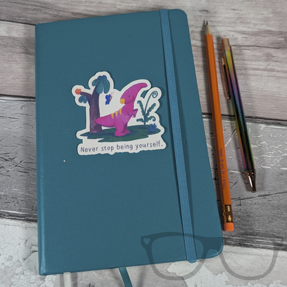  Irene the Parasaurolophus "Never stop being yourself" sticker placed on a notebook, adding a positive and inspirational touch to your workspace or study materials.