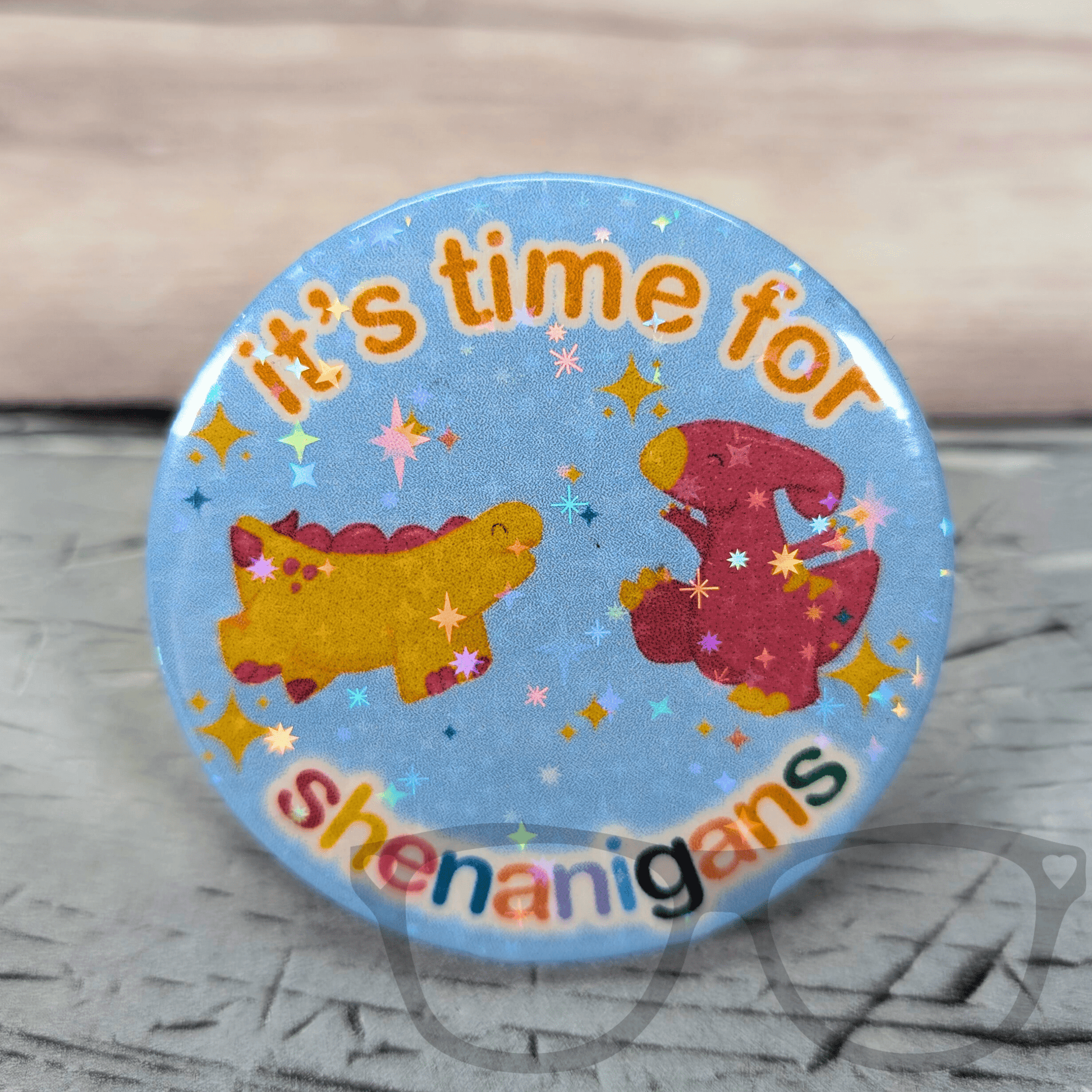 Blue 58mm pin badge featuring Derek the stegosaurus and Irene the parasaurolophus jumping for joy with "It's Time for Shenanigans" text, Mini Geek Boutique