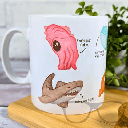 Mug with cartoon shark, pink octopus, and text on a wooden coaster.