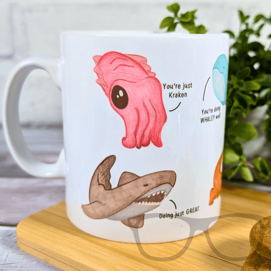 Mug with cartoon shark, pink octopus, and text on a wooden coaster.