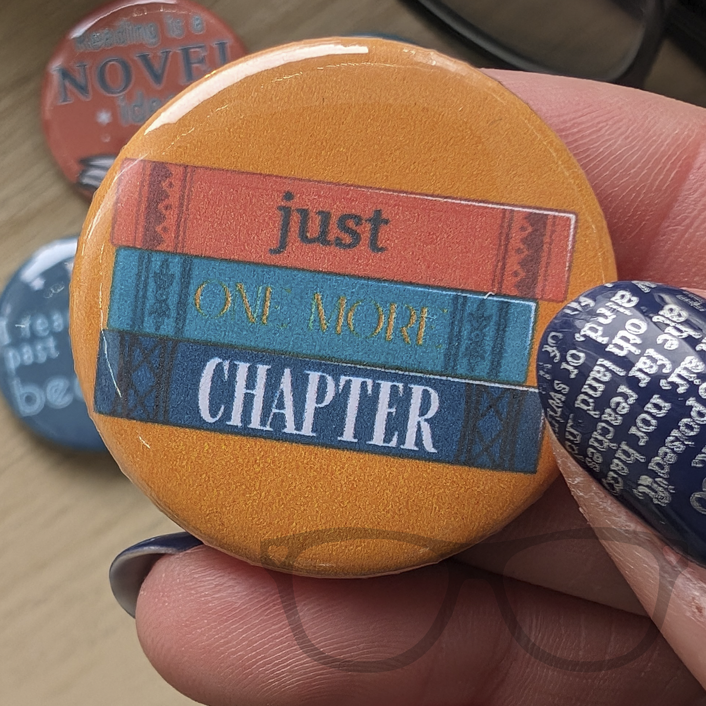 A yellow 38mm badge as part of a set "Just one more chapter"