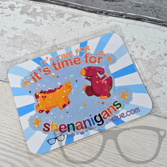 The “It’s Time for Shenanigans” dinosaur vinyl sticker is displayed in recyclable, eco-friendly packaging, ready for gifting or popping in the post.