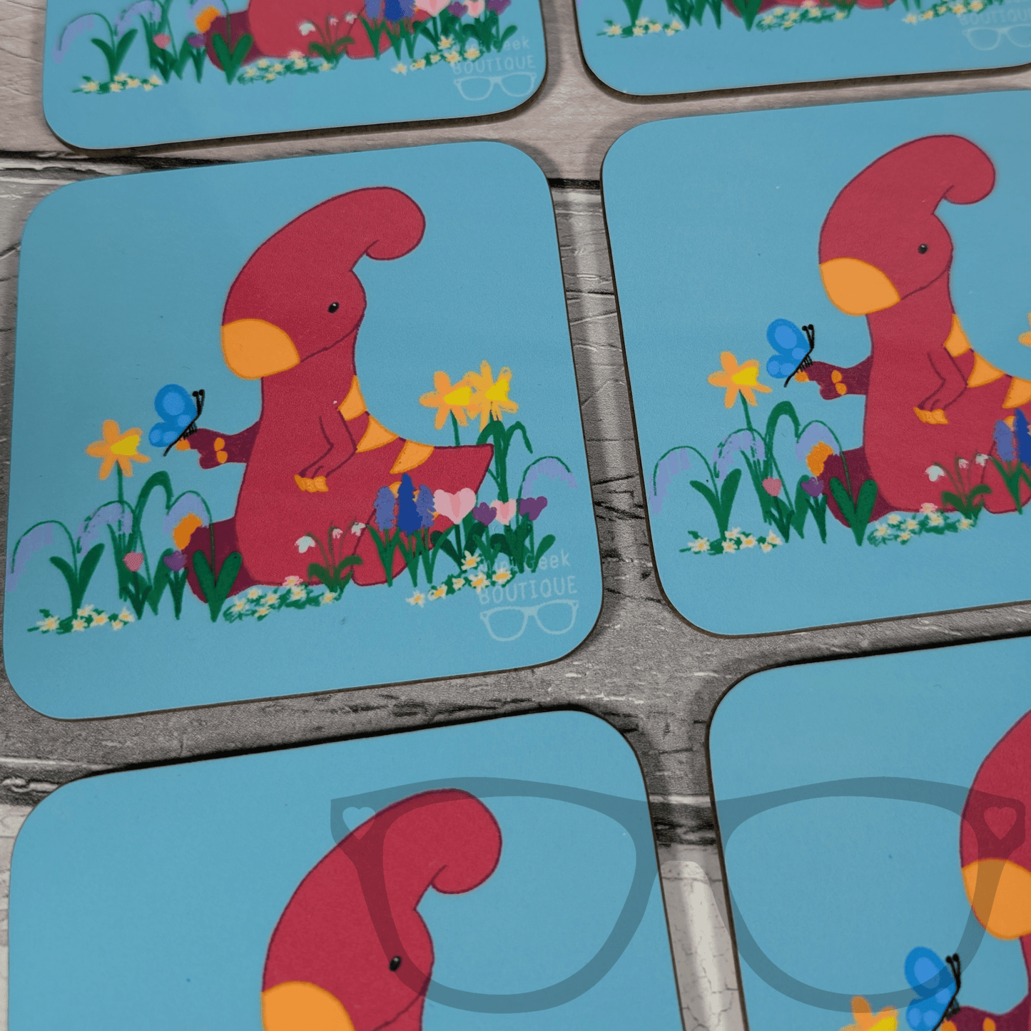 Mini Geek Boutique blue square drink coaster with Irene the pink parasaurolophus in a field of flowers