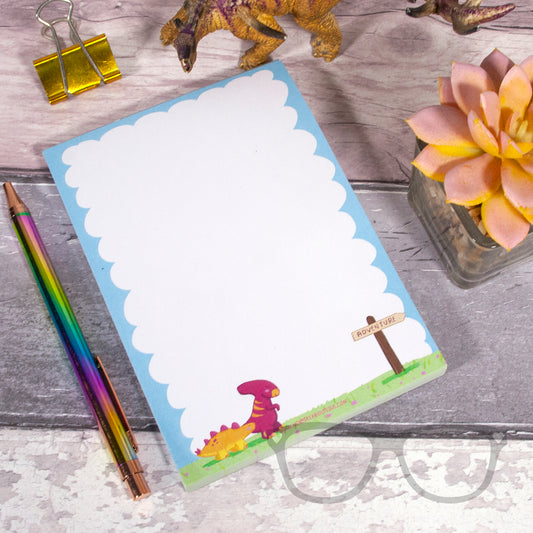 A6 plain notepad with dinosaur illustration, the dinosaurs are walking towards a sign which reads "Adventure " and is pointing to the right of the page.