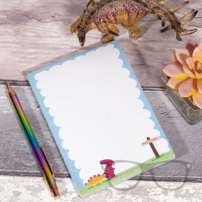 A6 plain notepad with an illustrqation of dinosaurs walking towards a sign that points to the right of the page sand says "Adventure"