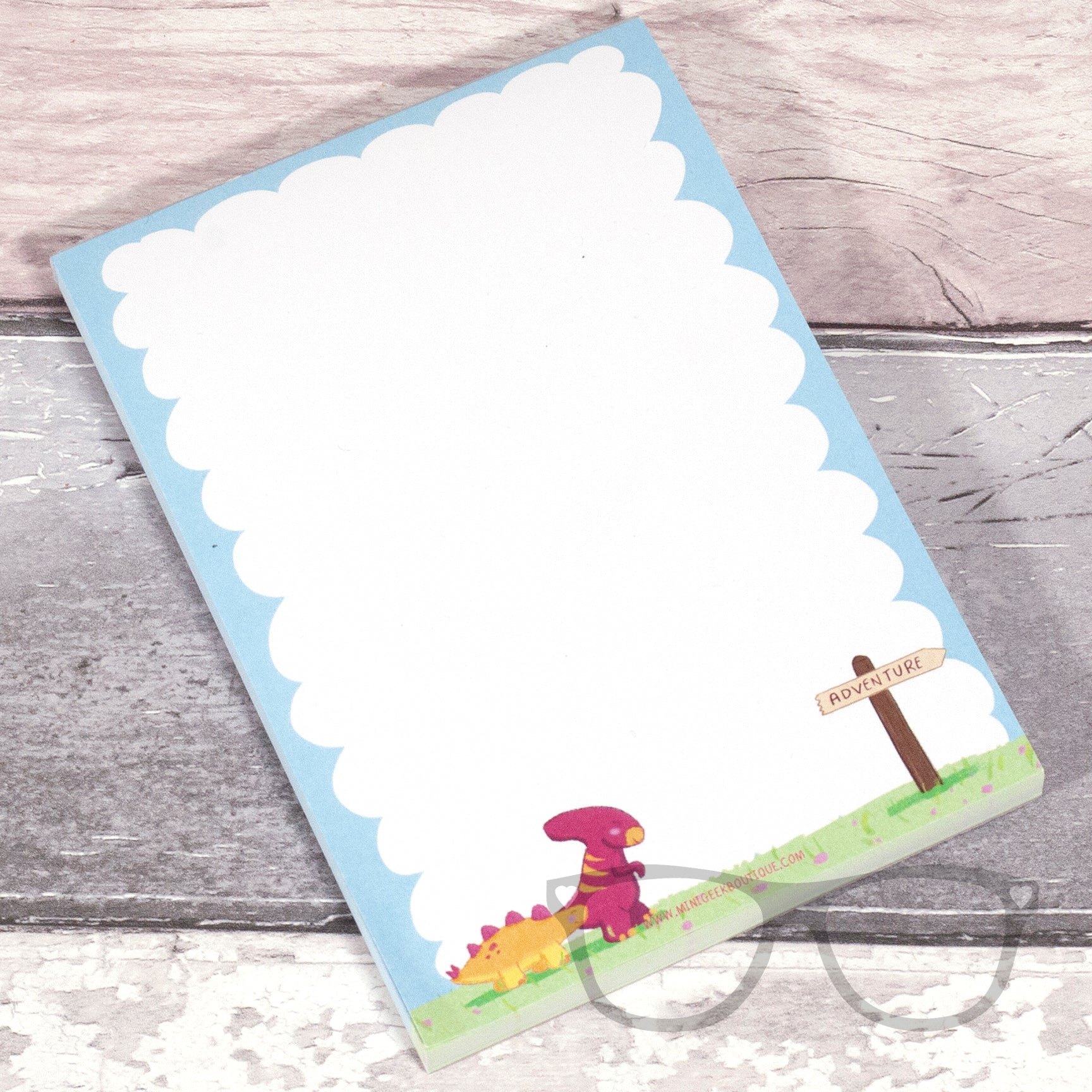 The white plain A6 sized notepad with dinosaur illustrations walking towards an adventure sign