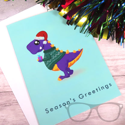 Dinosaur Christmas Card showing a t.rex holding a gift and wearing a festive winter jumper