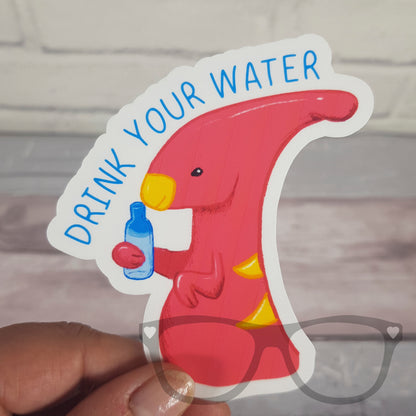 Irene the Dinosaur 'Drink Your Water' vinyl sticker being held, perfect for decorating water bottles, notebooks, and laptops to encourage healthy hydration habits